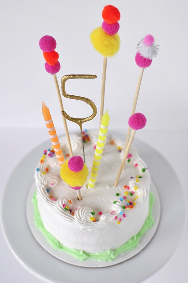 Adorable and simple, see how to create this Pom Pom Birthday Cake Topper for your next party!  Fun Banner Cake Toppers make celebrations so much more fun and they are easy to add to any dessert. Delineate Your Dwelling #pompombirthdaycake #pompomcaketopper #birthdaytopper #pompomcake