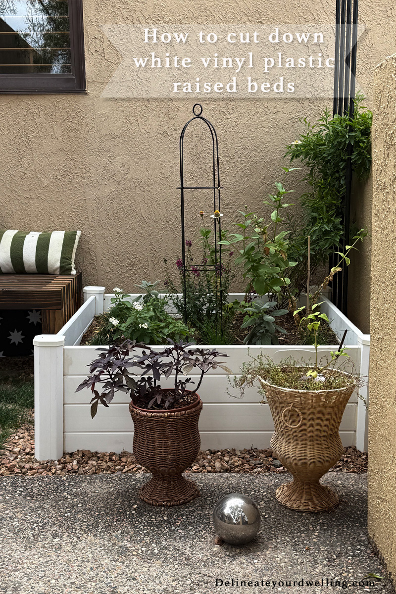 White vinyl raised garden bed with flowers and herbs growing in it inside a wall courtyard