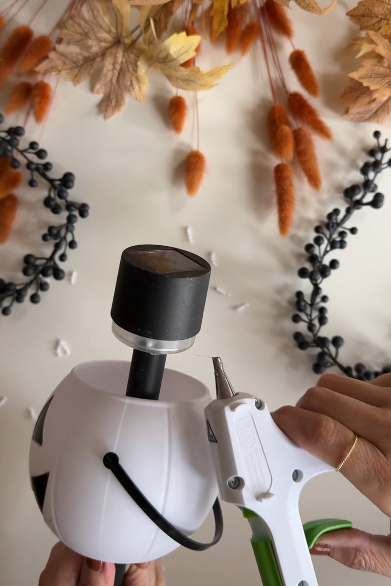 Hot gluing a solar light to the bottom of a white mini pumpkin