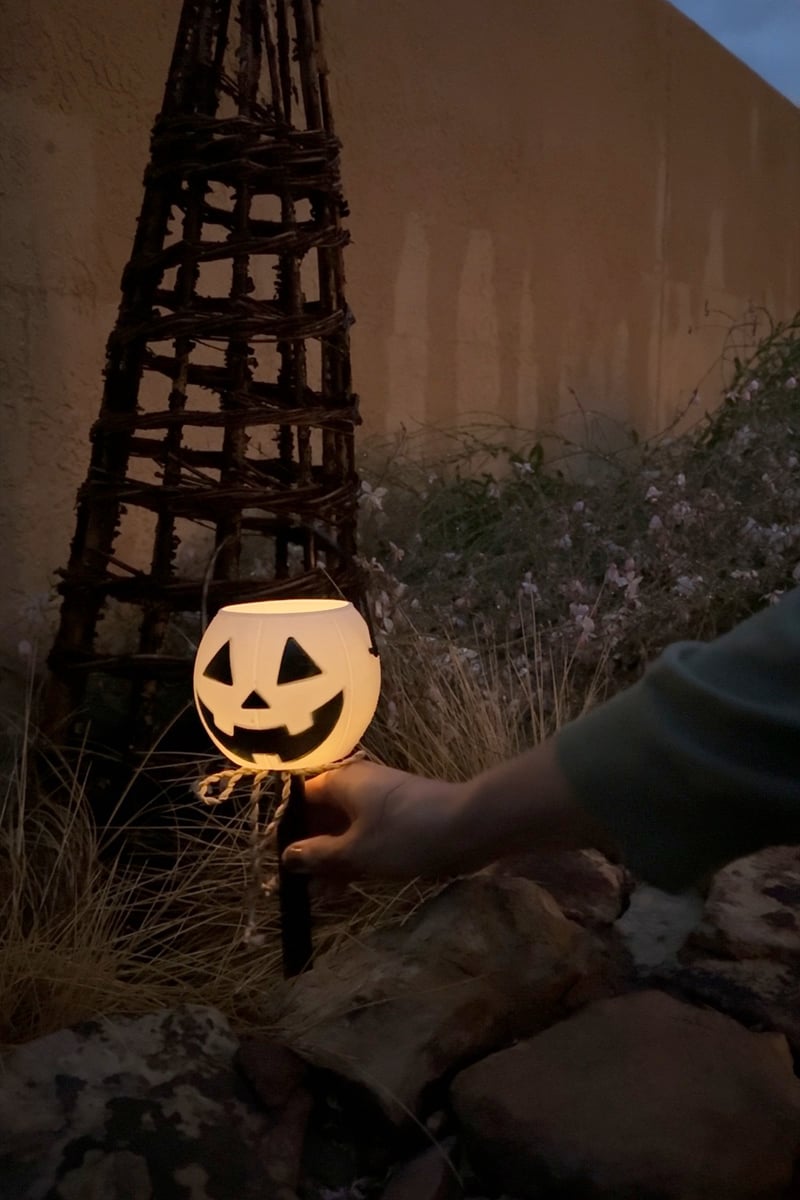 Glowing white pumpkin light in a bed of grasses and flowers for Halloween