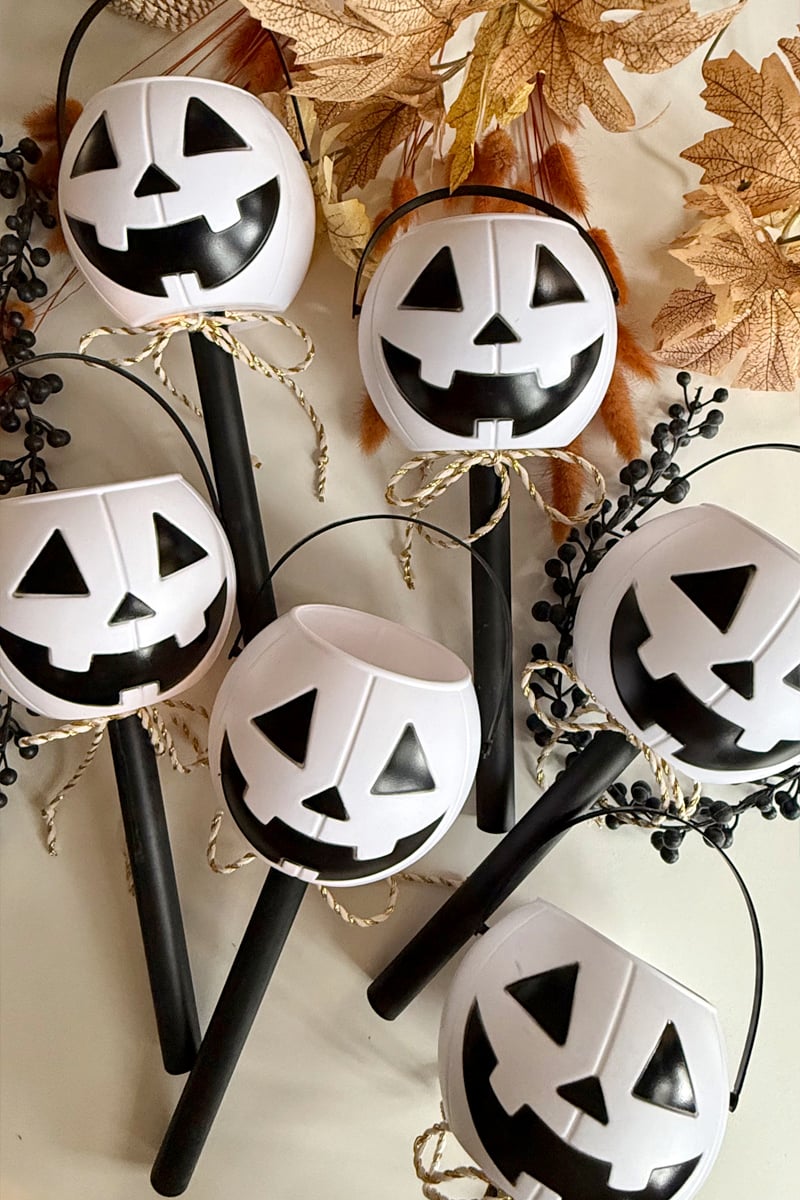 Six white mini plastic pumpkins turned into solar night time lights with cute gold and white ribbons sitting in a white table with fall decor and leaves all around