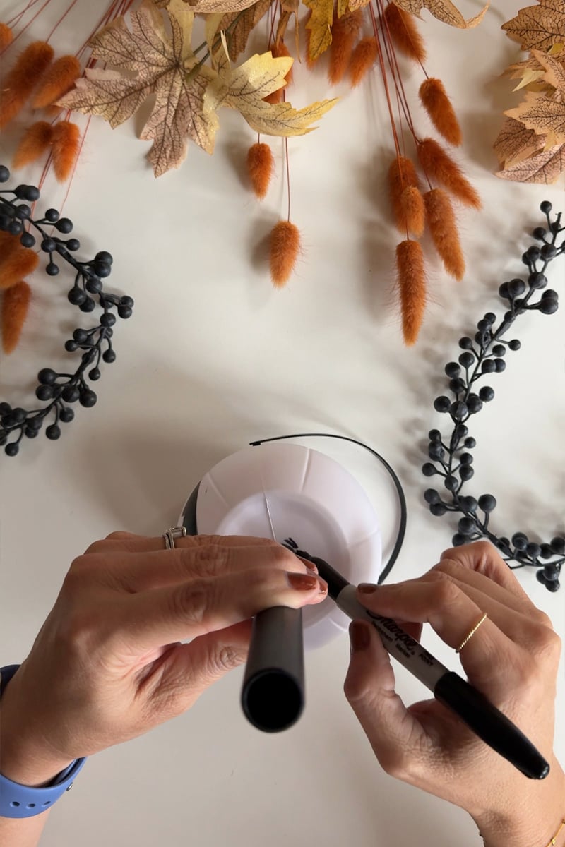 Tracing a circle with sharpie to the bottom of a white mini pumpkin