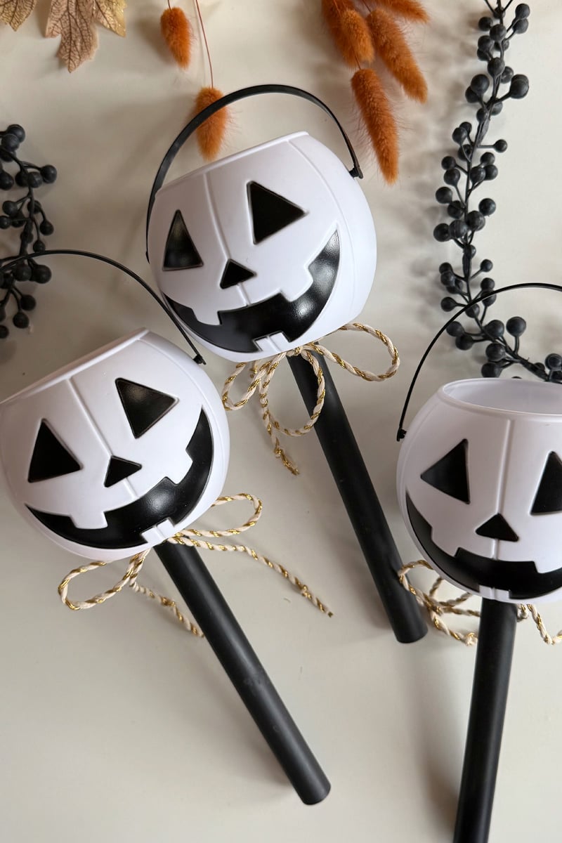 Three white mini pumpkins on black posts with gold and white ribbon
