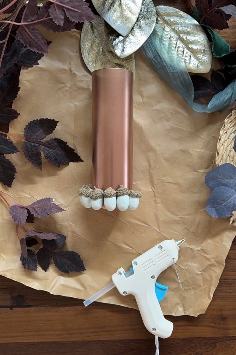 White painted acorns being glued to copper vase