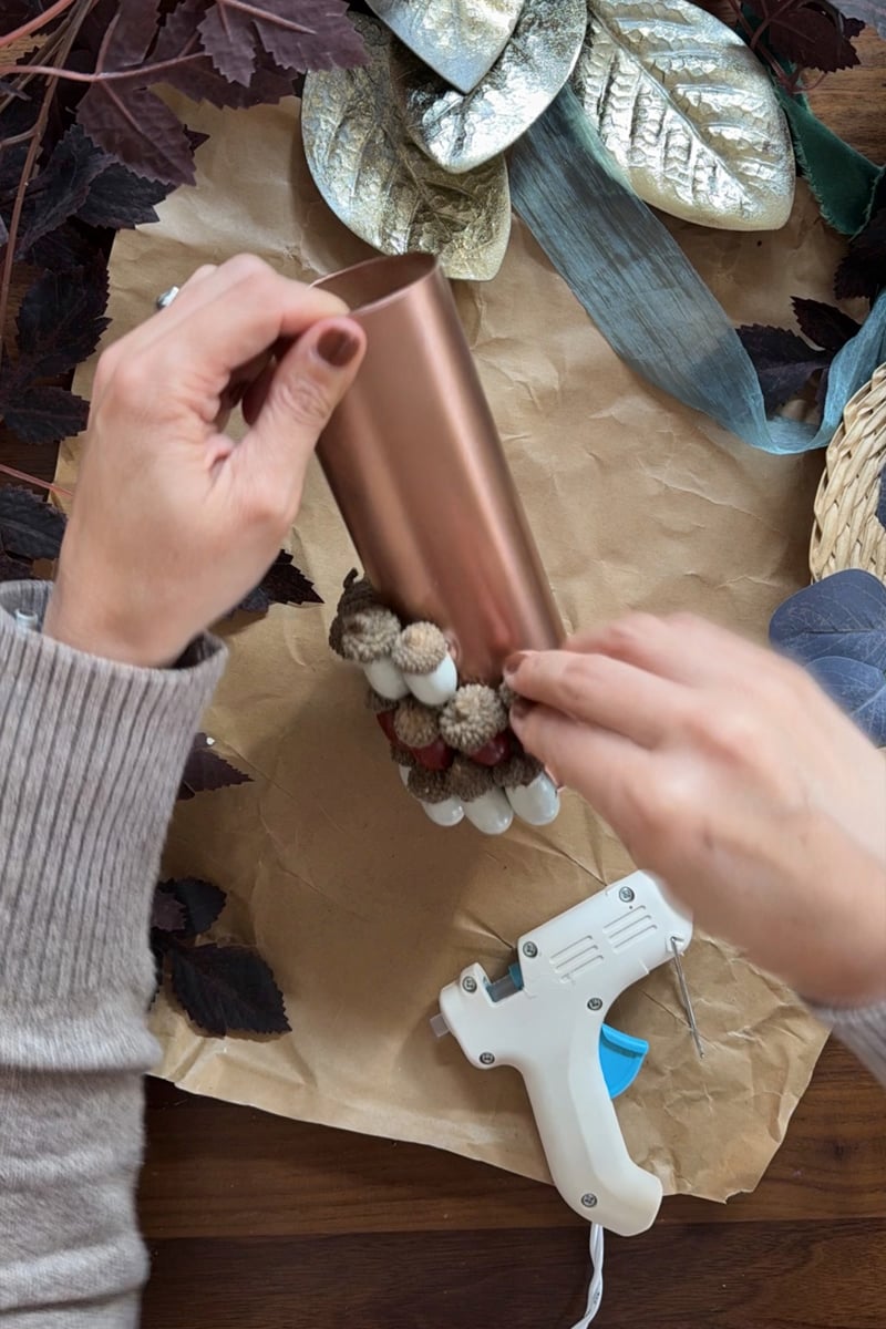 Hot gluing white painted acorns onto a glass vase