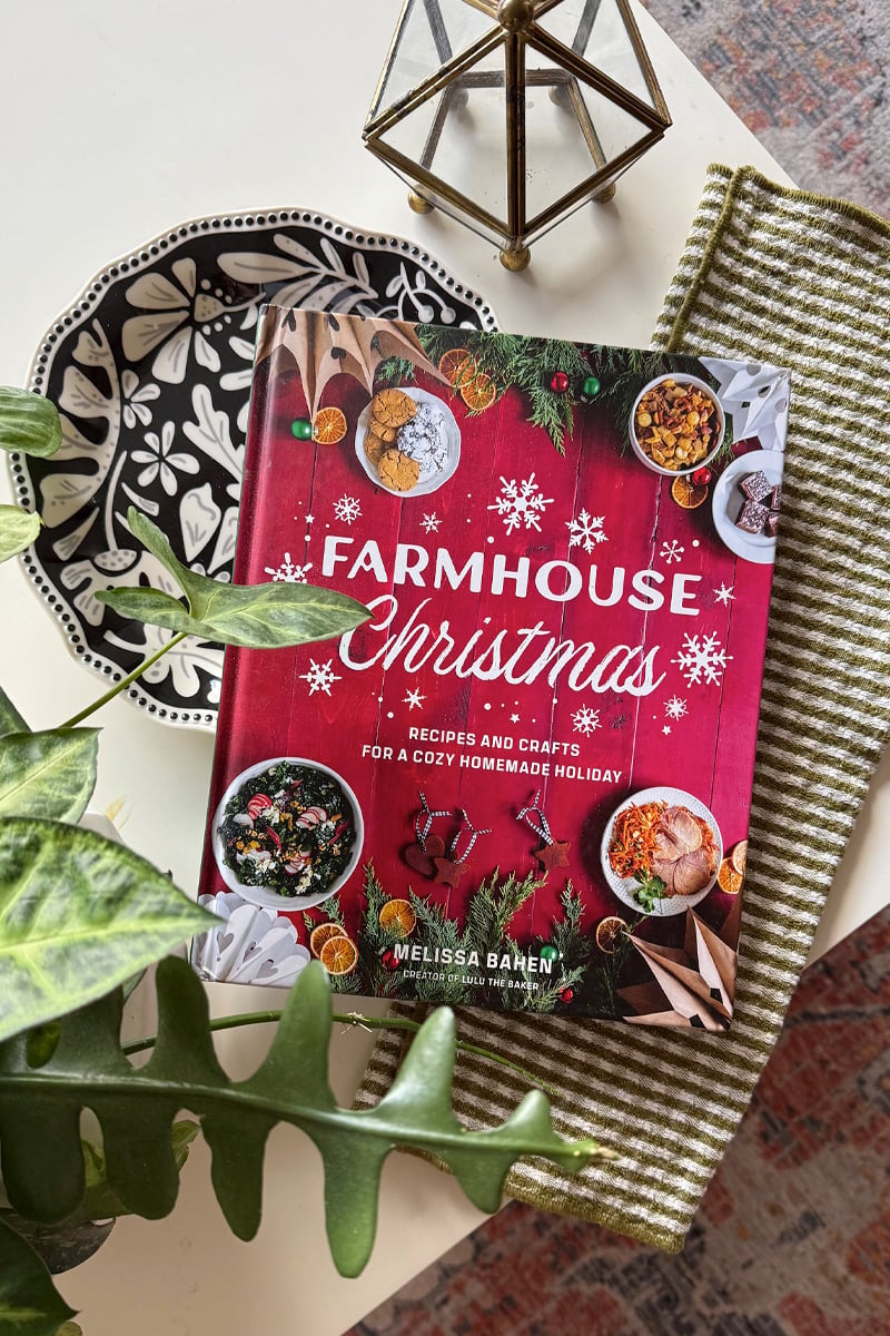 Red Farmhouse Christmas book styled on white coffee table with holiday decor surrounding it
