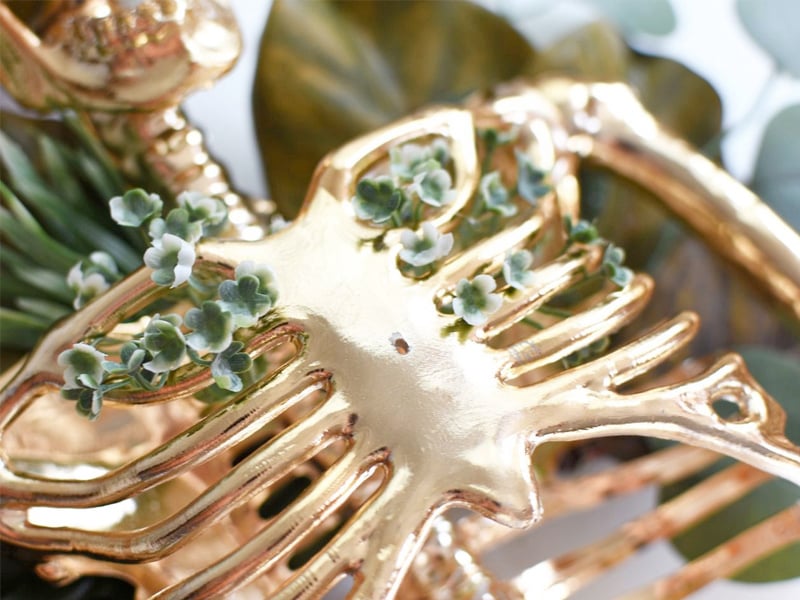 Small green flowers intertwined into a gold skeleton ribcage