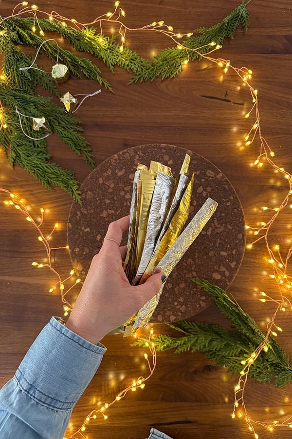Woman's hand holding pile of embossed silver and gold strips with twinkle lights