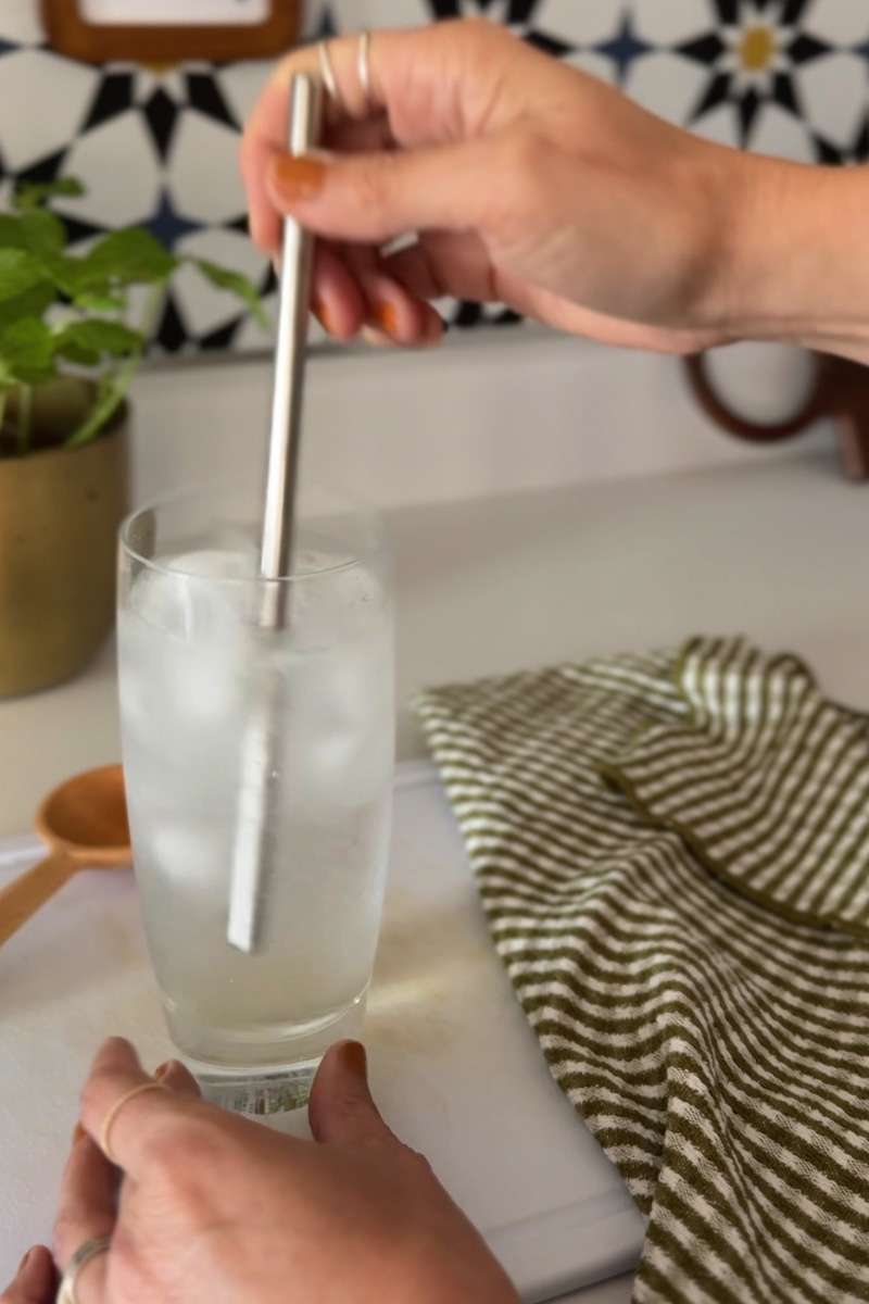 Metal straw stirring glass of ice and sparkling water