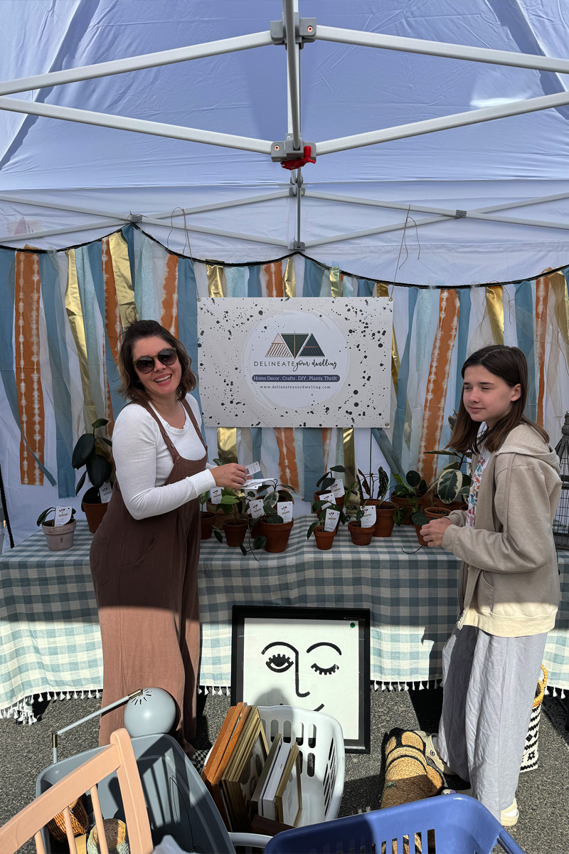 Two women setting up a craft show tent display selling plants