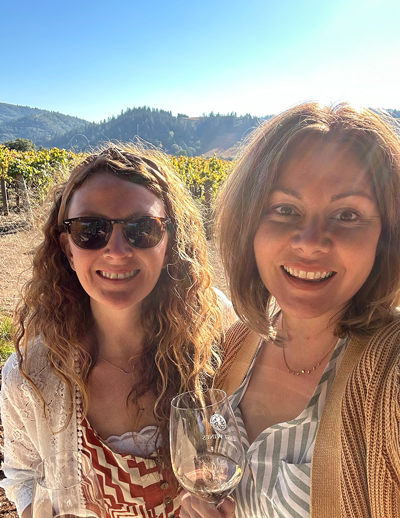 Two sisters enjoying a glass of wine in front of grape vines in Sonoma Country