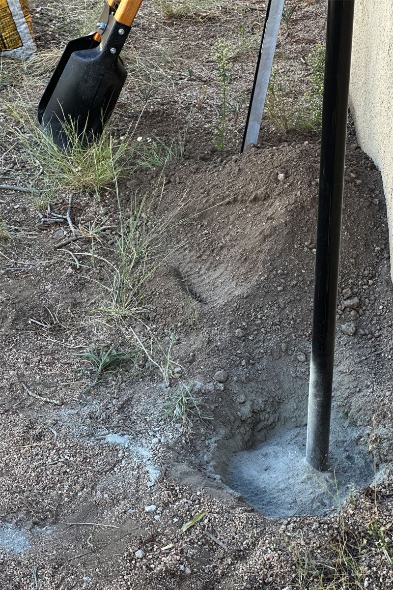 Hole in ground with a black pole filled with dry concrete mixture